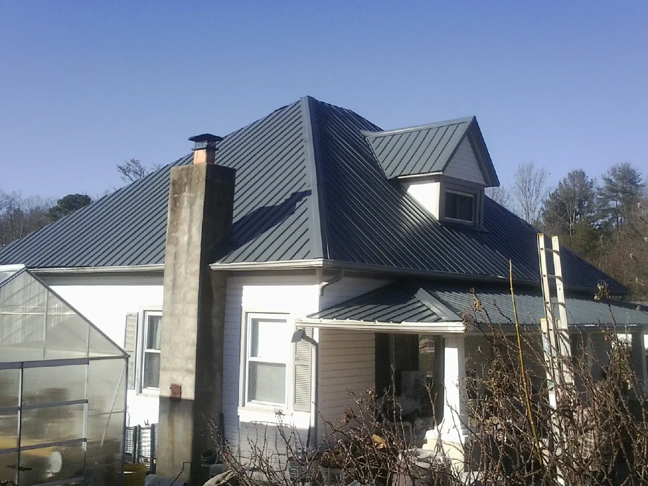 Dark blue standing seam metal roof on a white farmhouse with dormer — Slate & Tile Roof Repair by Roofing Brothers in Wauneta