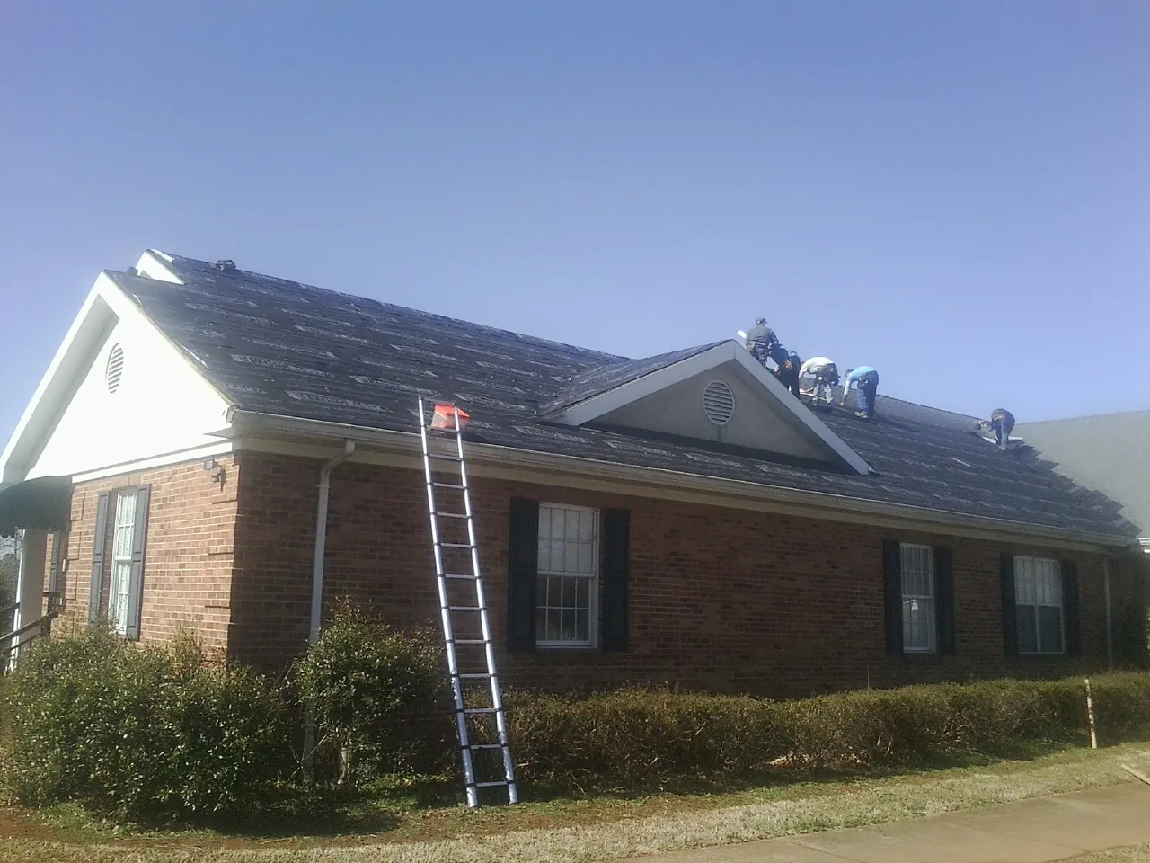 Crew tearing shingles off a brick ranch roof with a ladder set — Emergency Roof Repair work by our crew in Wauneta