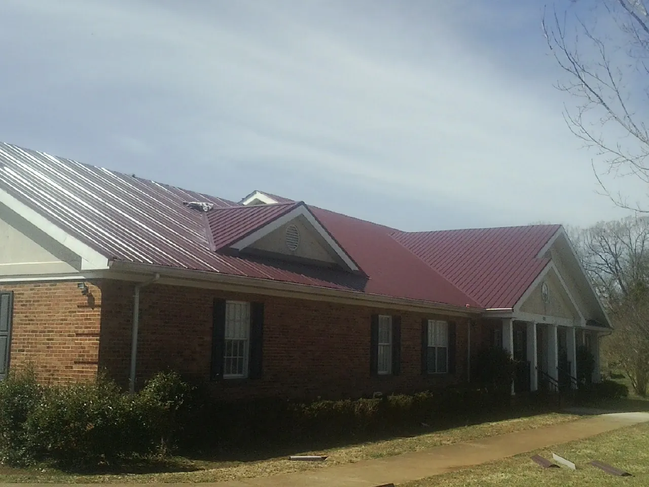 Red metal roof with gabled entries on a long brick building, from a Hail Damage Roof Repair job in Wauneta
