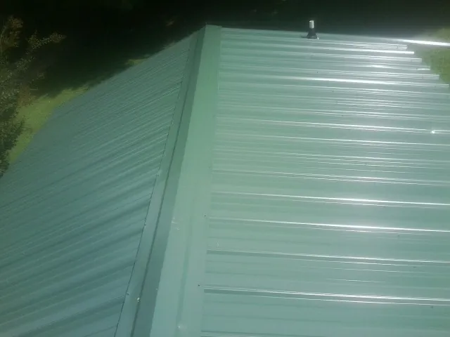 New green metal panels meeting at the ridge of a roof — Flat Roof Repair work by our crew in Wauneta