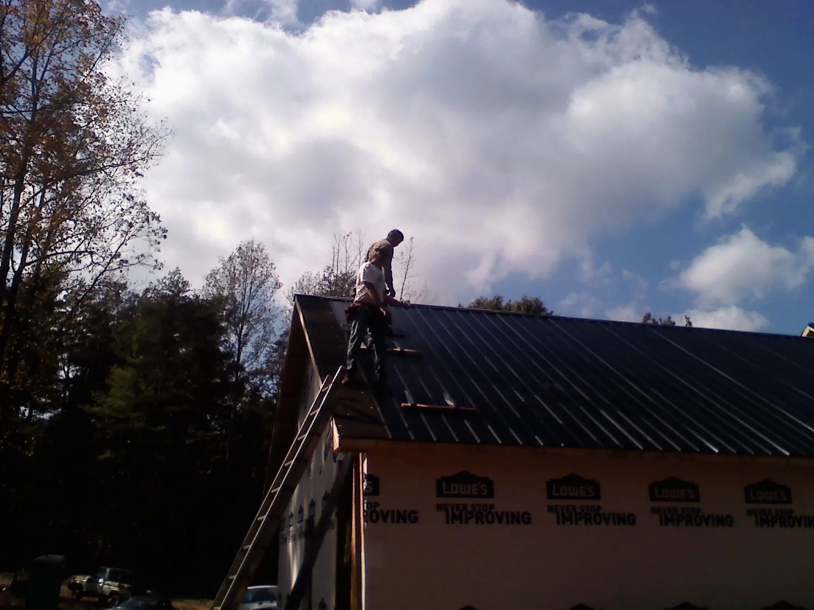 Roofer fastening dark metal panels high against a cloudy sky, from a Roof Inspection job in Wauneta
