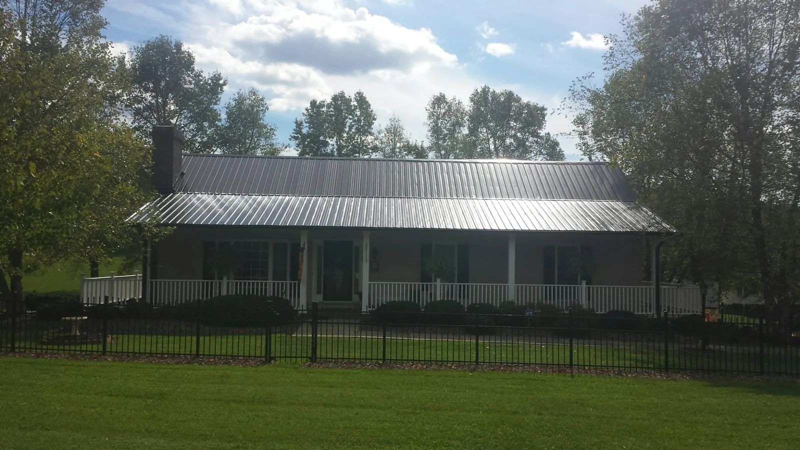 Gray metal roof on a brick ranch with a full width front porch — Gutter Guard Installation work by our crew in Wauneta