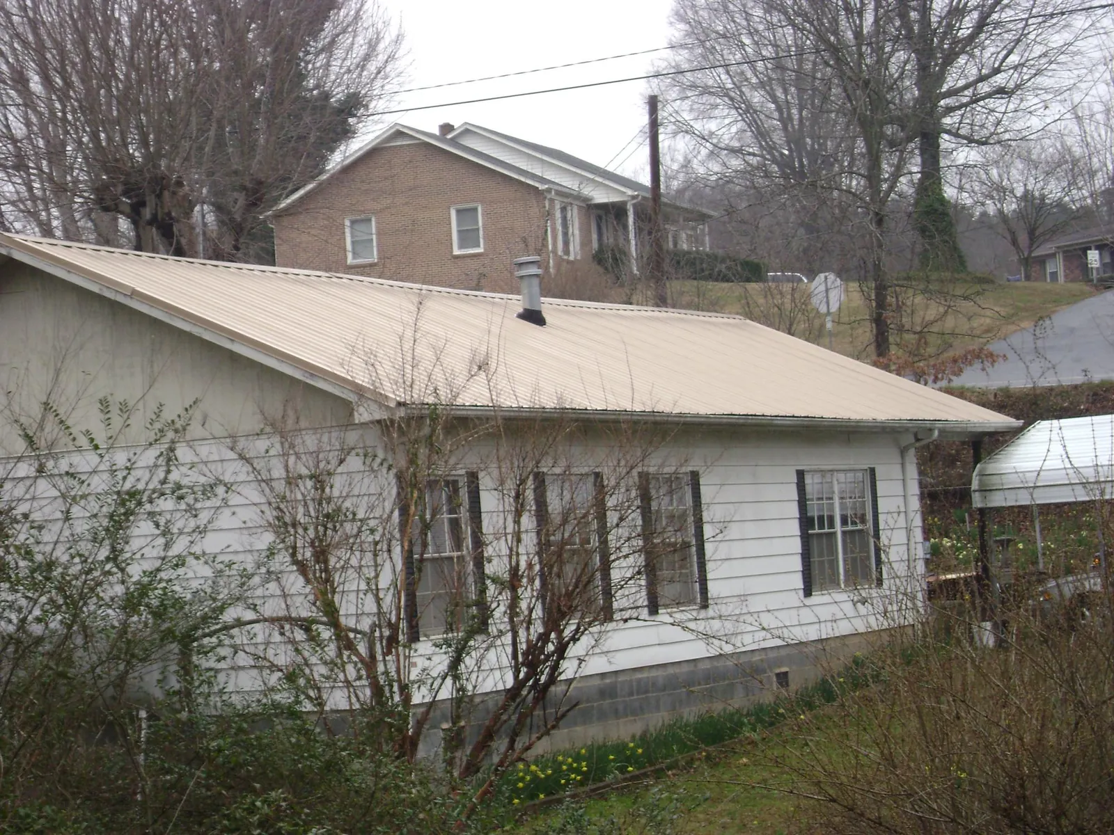 Tan metal roof on a white sided house set into a hillside — Commercial Roofing by Roofing Brothers in Wauneta